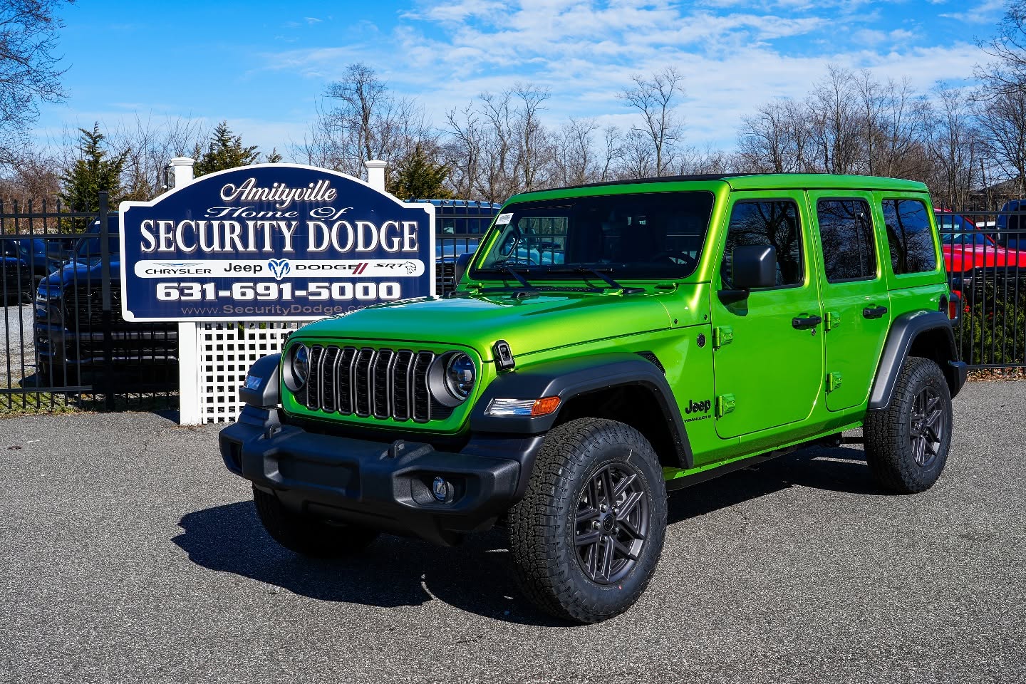 Green Jeep Wrangler displayed near a Jeep dealership sign in Amityville, New York
